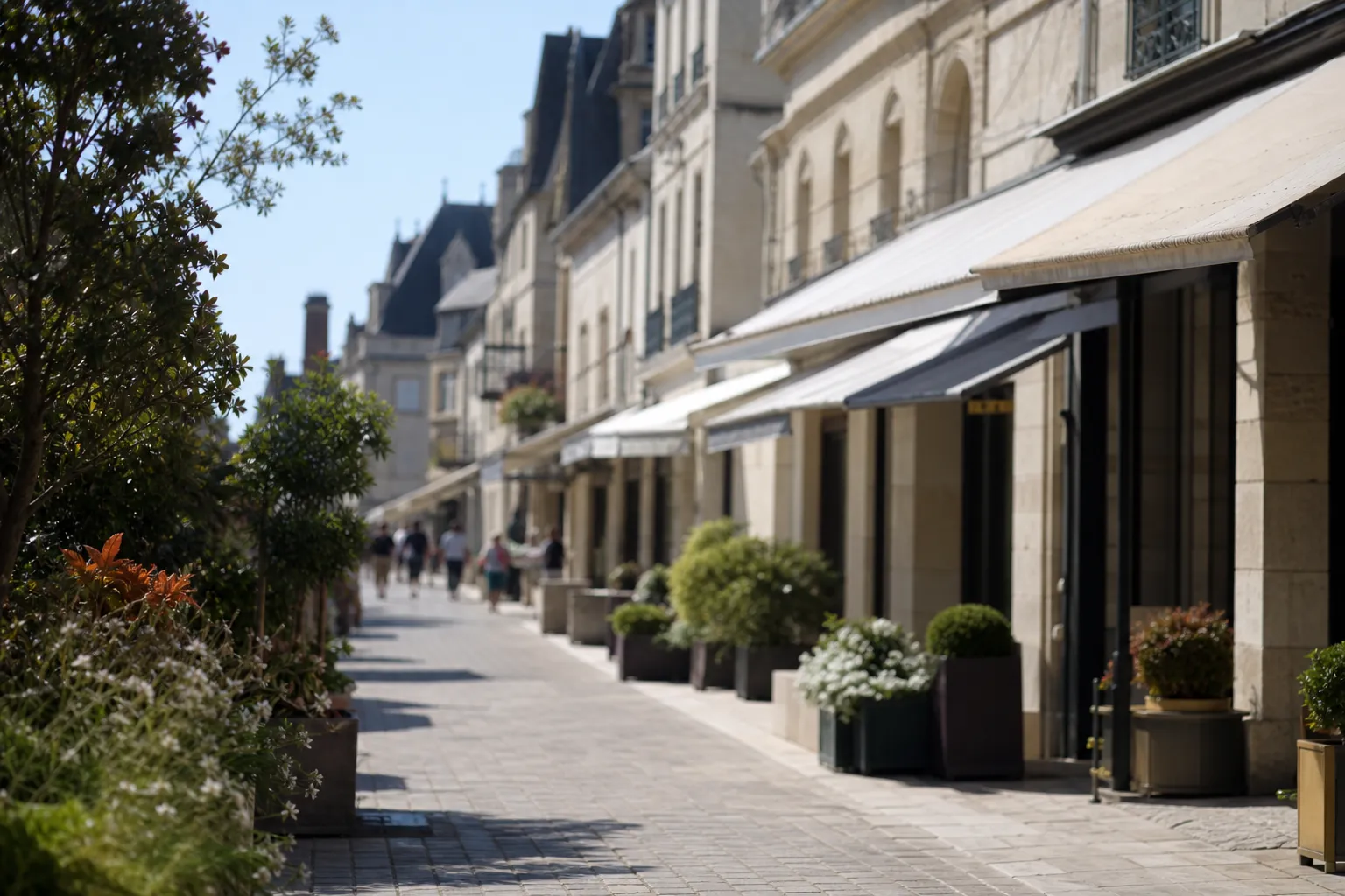 Rue commerçante d’un bourg tourangeau bordée de façades en tuffeau clair et de stores de toile